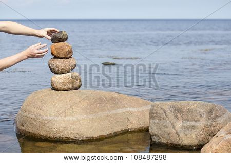 Human Hand Making Stack Of Large Round Stones Near The Water