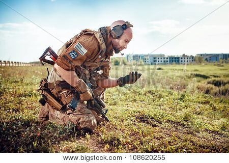 Military Pathfinder Is Looking At The Soil In His Hand. Ruined City On The Background.