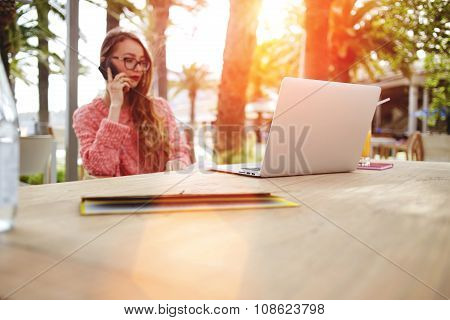 Smart female speaking on cell telephone while rest after work on laptop computer