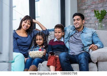 Happy young family eating popcorn while watching tv in living room