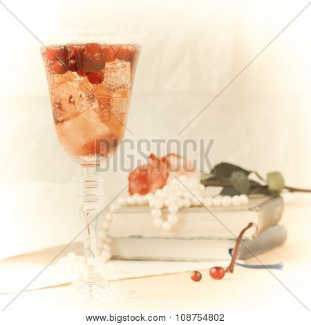 Glass Of Champagne And Cranberry Cocktail With Vintage Books And Pearls