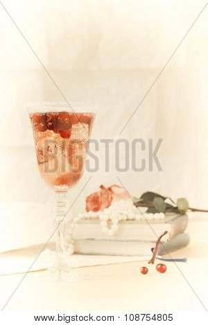 Glass Of Champagne And Cranberry Cocktail With Vintage Books And Pearls