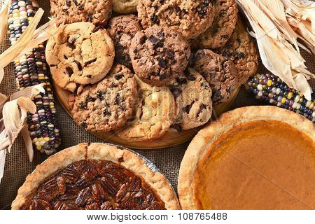 Closeup of pies and cookies for a Thanksgiving Day feast desserts. Pecan Pie, Pumpkin Pie, Chocolate Chip, oatmeal raisin and indian corn adorn the table.