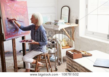 Female Artist Working On Painting In Studio