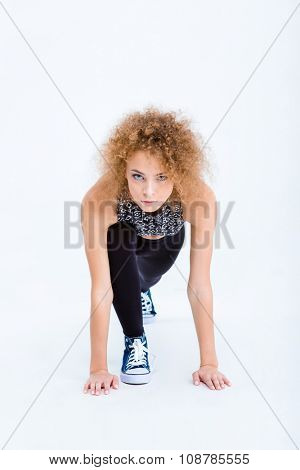 Portrait of a sports woman with curly hair standing in start position for running isolated on a white background