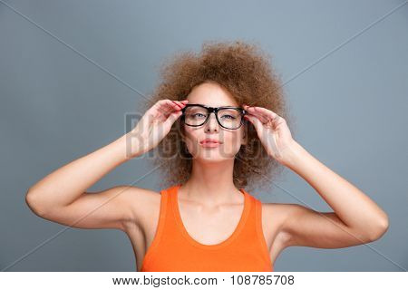 Portrait of confident young beautiful concentrated female with voluminous curly hairstyle in black glasses