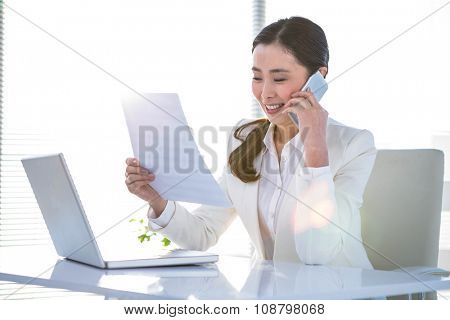 Smiling businesswoman on phone reading documen at the desk in work