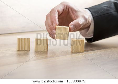 Male Hand Placing Four Wooden Cubes In A Row.