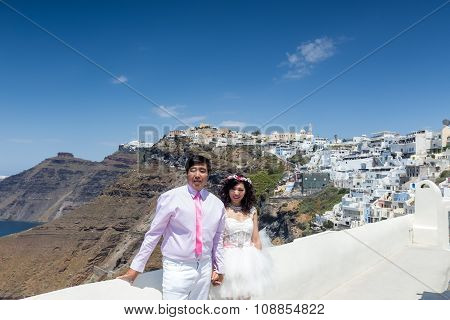A Couple Of Newlywed’s Tourists Pose On A Balcony With The View Of Santorini Island, In Greece. Tour