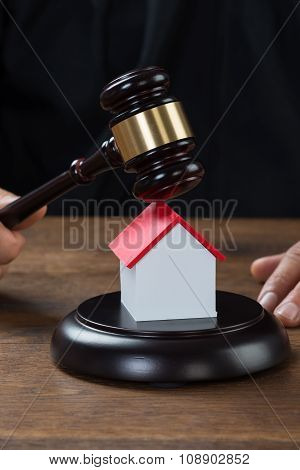 Judge Holding Gavel On House At Desk