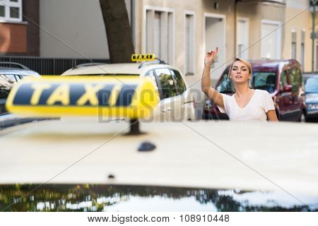 Woman Raising Arm To Hail Taxi On Street