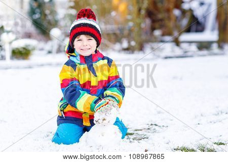 Beautiful kid boy in colorful clothes making a snowman