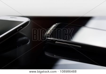 A White And A Black Smartphone With Reflection On A Tablet