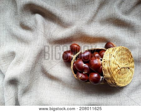 Little wicker basket with chestnuts on beige pleated fabric