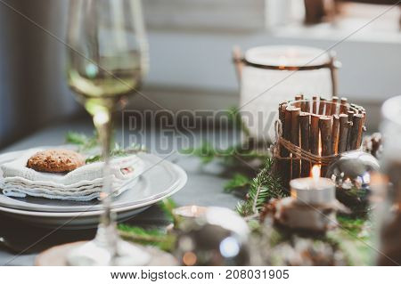 Festive Christmas and New Year table setting in scandinavian style with rustic handmade details in natural and white tones. Dining place decorated with pine cones branches and candles