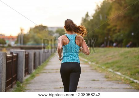Young sporty woman running in park. Fitness girl jogging in park. Rear view of sporty girl running on embankment