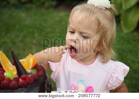 Girl birthday. A little white-haired girl of two years is trying a birthday cake. Little girl celebrating second birthday.