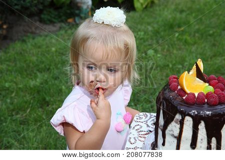 Girl birthday. A little white-haired girl of two years is trying a birthday cake. Little girl celebrating second birthday.