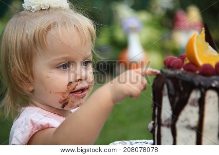 Girl birthday. A little white-haired girl of two years is trying a birthday cake. Little girl celebrating second birthday.