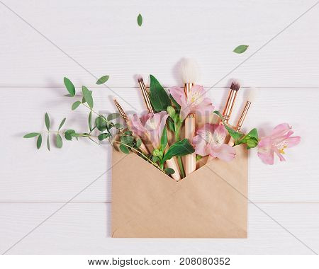 Decorative flat lay composition with makeup products, kraft envelope and flowers. Flat lay, top view on white background. Copytext