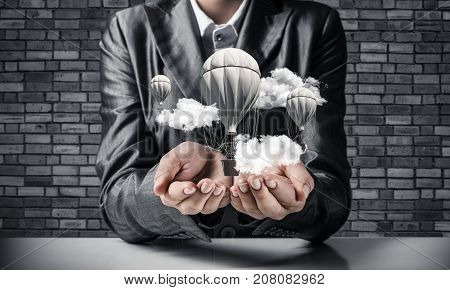 Closeup of business woman in suit presenting flying aerostate among clouds in her palms with dark brick wall on background. 3D rendering.