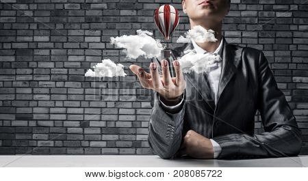 Closeup of business woman in suit presenting flying aerostate among clouds in her palm with dark brick wall on background. 3D rendering.