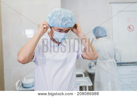 Young doctor during preparation for operation. Assistant of surgeon wearing surgical mask in operation room at the hospital
