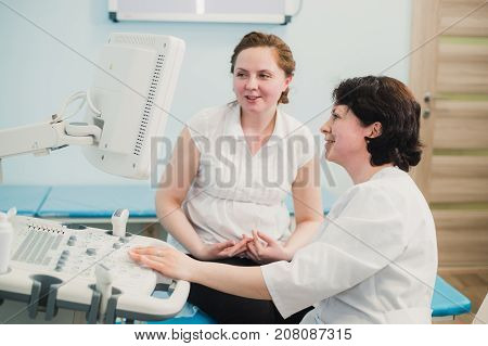 Pregnant woman looking at ultrasound shots of her growing baby showed by her doctor during medical examination.