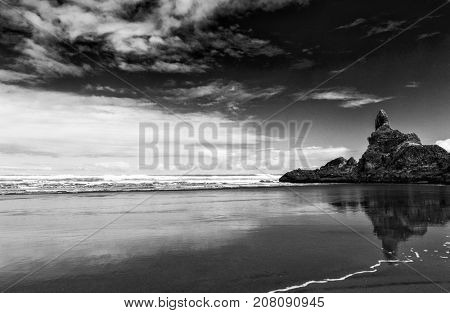 Reflection of rocks in the wet sand on the beautiful Piha beach near Auckland, New Zealand. Dramatic balck and white