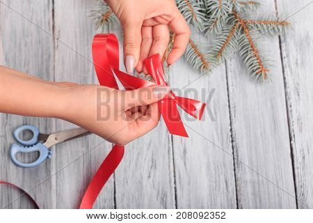 Hands with scissors. Red ribbon. Close-up. Next to it is a branch of spruce.