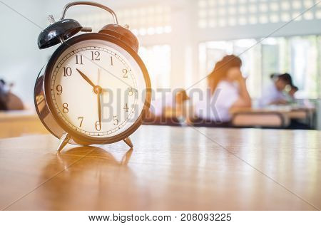 Closeup of Retro alarm clock with ten o'clock on table teacher in blur students exams classroom. Time is indefinite continued progress of existence. Education concept selective focus.