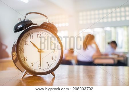Closeup of Retro alarm clock with ten o'clock on table teacher in blur students exams classroom. Time is indefinite continued progress of existence. Education concept selective focus.