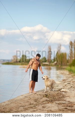 A young man with muscular body runs on the beach with his friend dog. An owner and dog walking on a nature background.