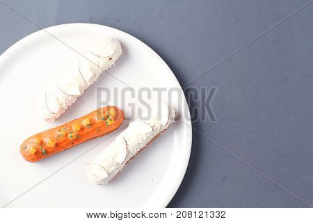 pumpkin orange eclair and white coconut eclairs on a white plate and grey table
