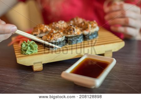 The girl smiles and eat Japanese food keeps sushi rolls with wooden chopsticks and moka them in soy sauce