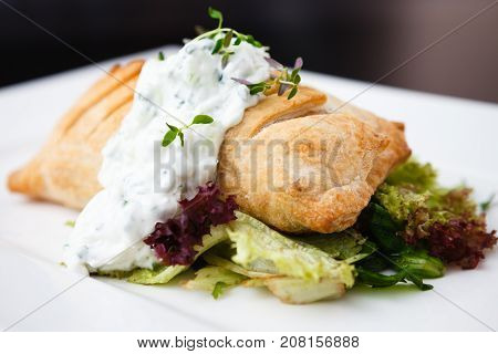 Traditional russian pie - coulibiac. Baked puff pastry filled with smoked salmon, served with sour cream sauce
