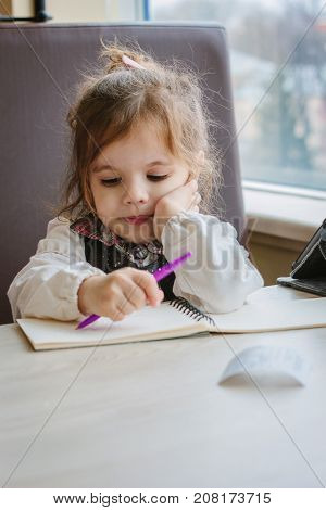 Little kid girl writing or drawing with pen in scetch book.
