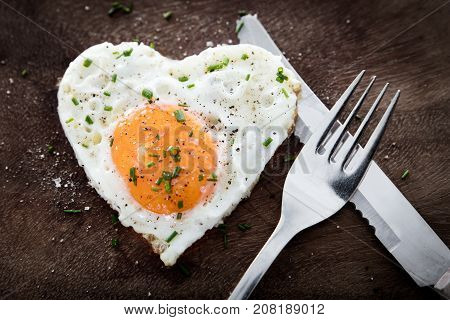 Fried Egg With Heart Shape And Cutlery On Wooden Background