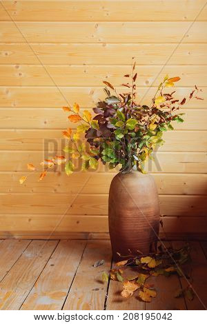 Autumn Still Life. Dried leaves in ceramic vase on wooden floor, on wooden background