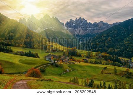 Colorful autumn scenery in Santa Maddalena village with church roads and meadows on foreground and mountain peaks on background at sunrise. Dolomite Alps South Tyrol Italy.