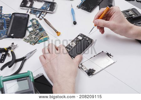 Repairman disassembling smartphone with screwdriver. Technician fixing broken phone, electronics repair service, repairer pov, copy space for text