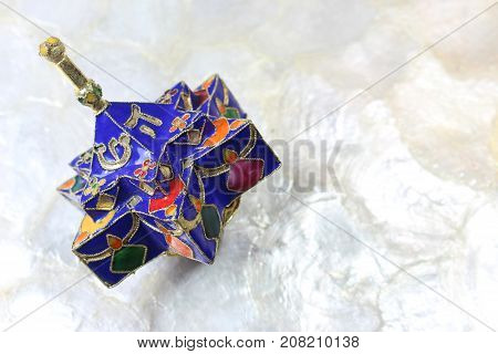 Enameled blue star shaped Hanukkah dreidel on a soft white background