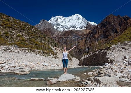 Woman is doing yoga excercises near big lake on the Manaslu circuit trak in Nepala