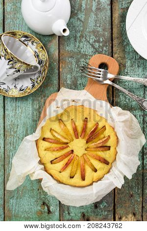 Tea time. Homemade tasty round cake with apples freshly baked in paper with teaware on robin egg blue background above view