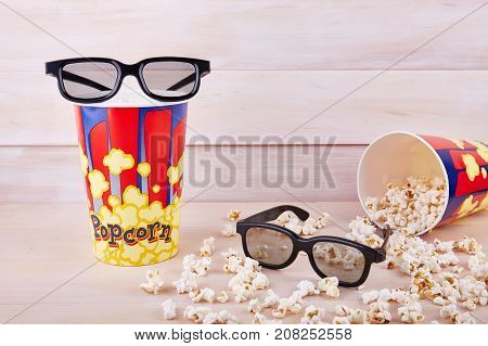 Bowl with scattered popcorn and 3D glasses on a wooden background