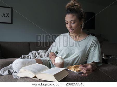 closeup of beautiful young mixed race Asian Caucasian woman reading book at home on couch with hot chocolatemilk and cookies