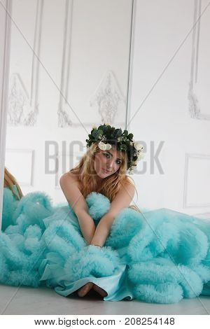 Beautiful young girl in cloud dress. Model with flowers in white room.