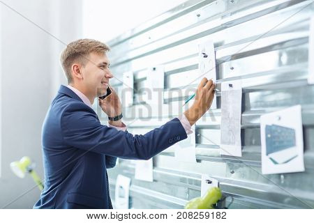 A young man speaks on the phone and takes notes at the office on a gray magnetic board. Close-up. A view from the side.