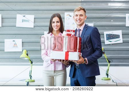 Young happy employees are standing with gifts in the office. They look at the camera. Close-up.