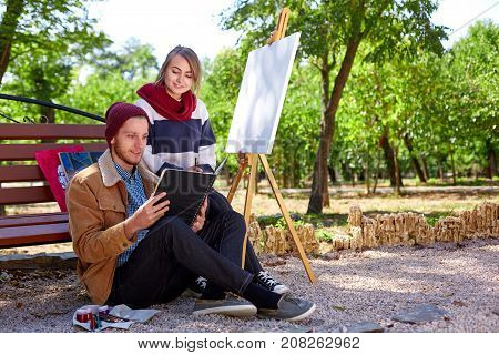 A young guy and a beautiful girl are watching pictures in their black album for drawing